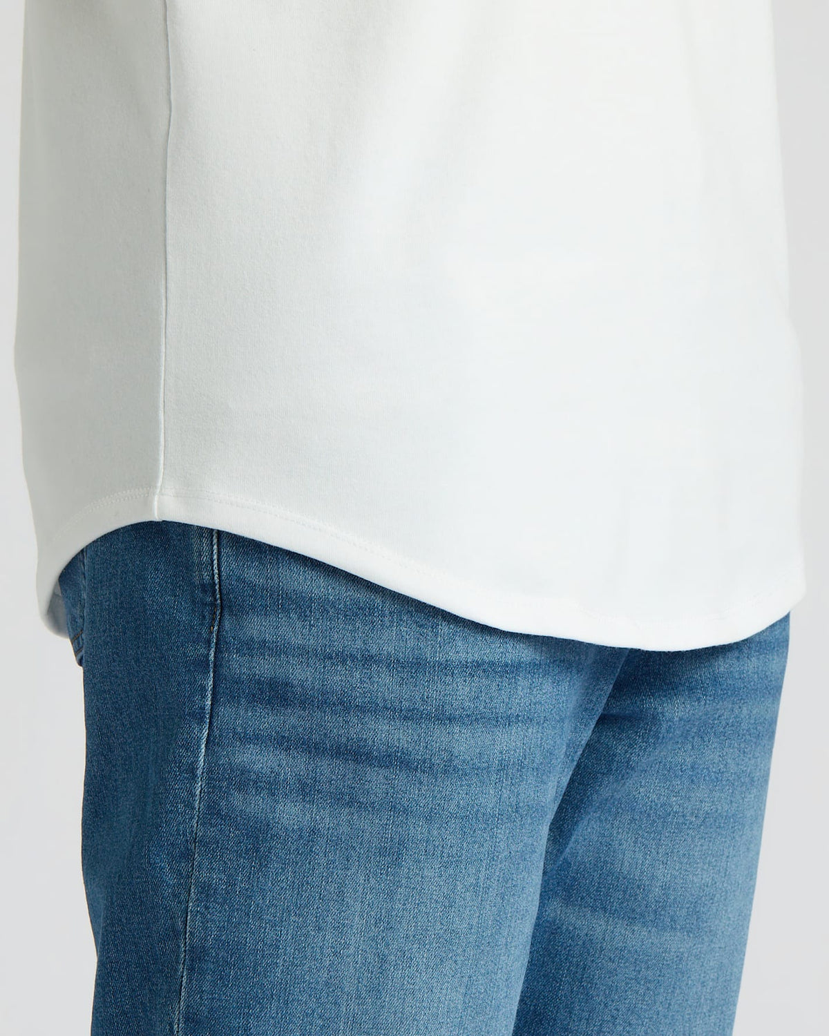 Close-up of the curved hem on the All White Tall Heavyweight Curved Hem Crew 3-Pack shirt worn over blue denim jeans, showing the heavyweight fabric and clean stitching in this men's basics essential.