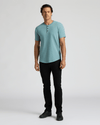Man wearing a light blue short-sleeve shirt with a three-button placket and curved hem paired with black pants and black shoes, showcasing the Heavyweight Curved Hem Henley 3-Pack.