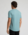 Rear view of a man wearing a light blue Citadel Heavyweight Curved Hem Henley, showcasing the curved hem and short sleeves, styled with black pants.