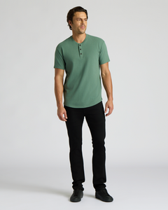 True ClassicMan wearing a green short-sleeve buttoned shirt and black pants, modeling the Heavyweight Curved Hem Henley 3-Pack in a casual, classic men's basics style.