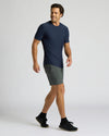 Man wearing a navy blue Active Curved Hem Crew 6-Pack t-shirt paired with gray athletic shorts and black sneakers, walking confidently against a plain background.