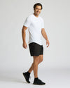 Man wearing All White Active Curved Hem Crew 6-Pack t-shirt, paired with black shorts and sneakers, smiling while walking against a plain light background.