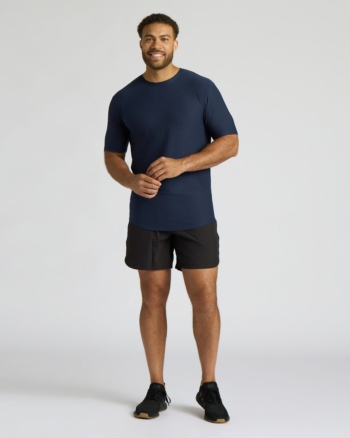 Man wearing a navy t-shirt and black shorts on a light gray background