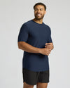 Man wearing a navy blue Tall Active Curved Hem Crew 3-Pack shirt and black shorts, standing smiling against a light gray background in a relaxed pose.