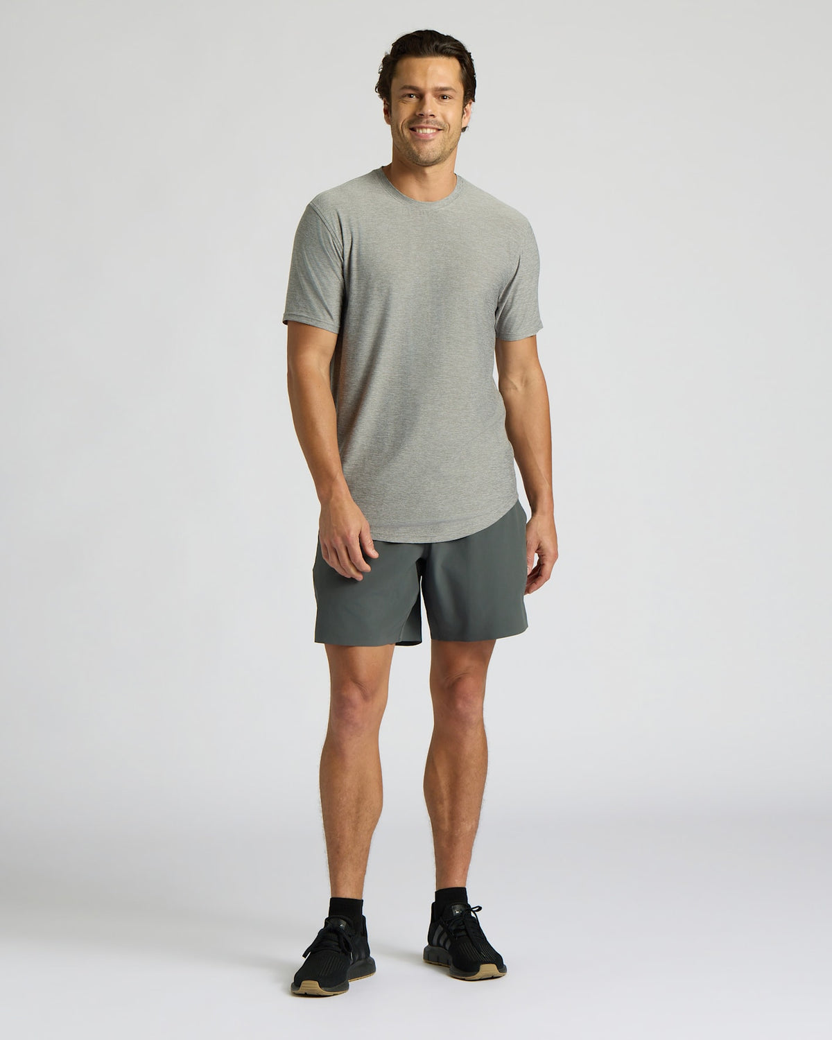 A man modeling a light gray short-sleeve crewneck t-shirt and dark gray athletic shorts, standing against a light gray studio background.