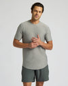 A man wearing a heather gray short-sleeve crewneck t-shirt and dark gray athletic shorts, standing against a light gray studio background.