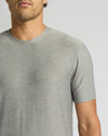 A close-up of a man wearing a light gray heather crew-neck t-shirt against a solid light gray background.