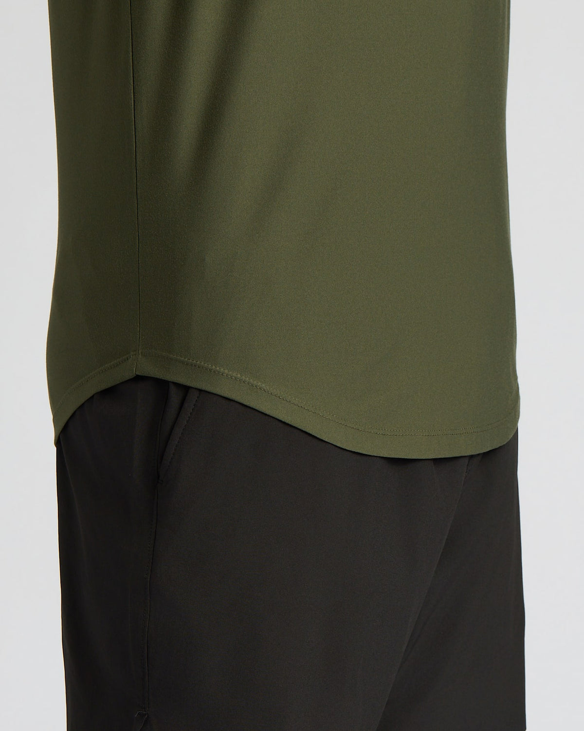 Close-up of a person wearing an olive green athletic top and black shorts against a light gray background.