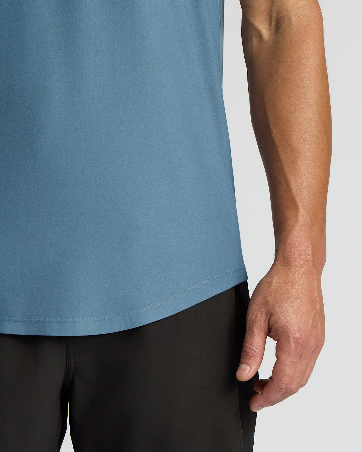 Close-up of a person wearing a muted blue athletic tank top and black shorts against a light gray studio background.