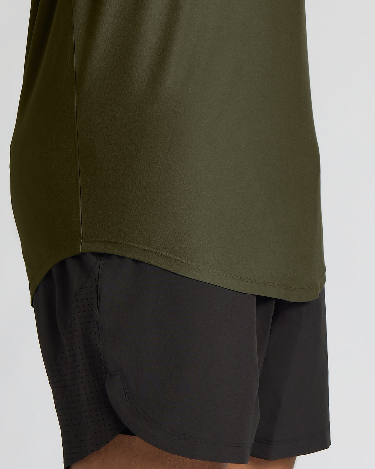 Close-up of a person wearing an olive green athletic top and black athletic shorts against a light gray background.
