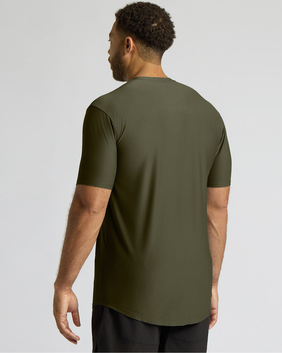 A man wearing a short-sleeve athletic t-shirt in olive green, shown from the back against a light gray studio background.