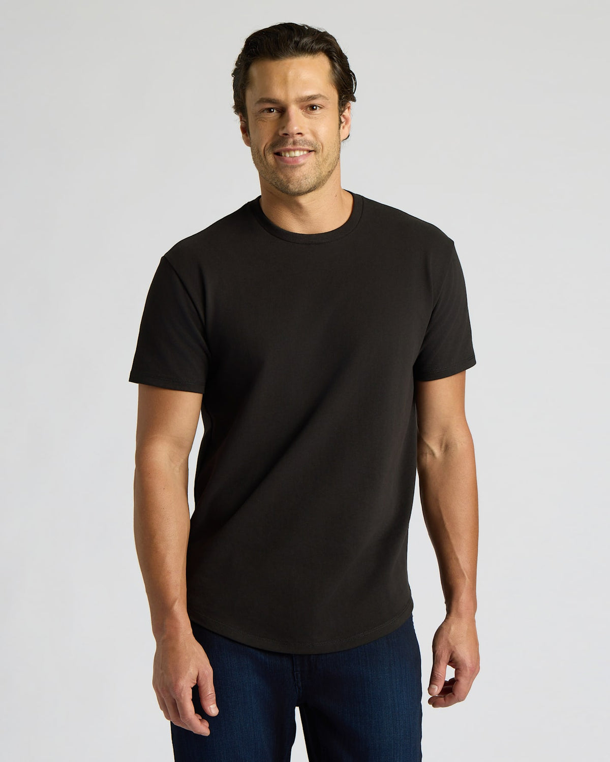 A smiling man wearing a black Heavyweight Curved Hem Crew 6-Pack t-shirt, styled as a classic men's basic with a curved hem and short sleeves.
