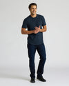 Man wearing a navy blue Heavyweight Curved Hem Crew 6-Pack t-shirt paired with dark jeans and black shoes, standing against a plain light background with a relaxed smile.