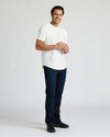 Man wearing a white Heavyweight Curved Hem Crew 6-Pack t-shirt paired with dark jeans and black shoes, standing and smiling against a plain background.