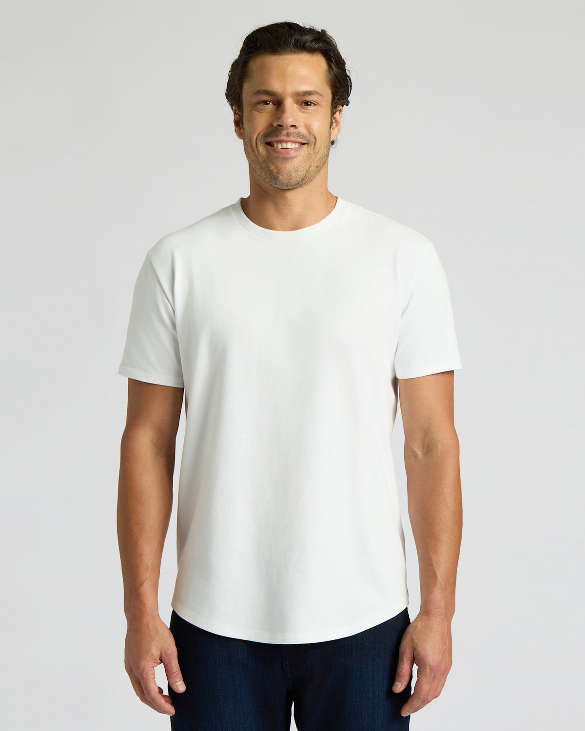 Man wearing a white Heavyweight Curved Hem Crew 6-Pack t-shirt, standing and smiling with a clean, minimal background, showcasing a classic men's basics style.