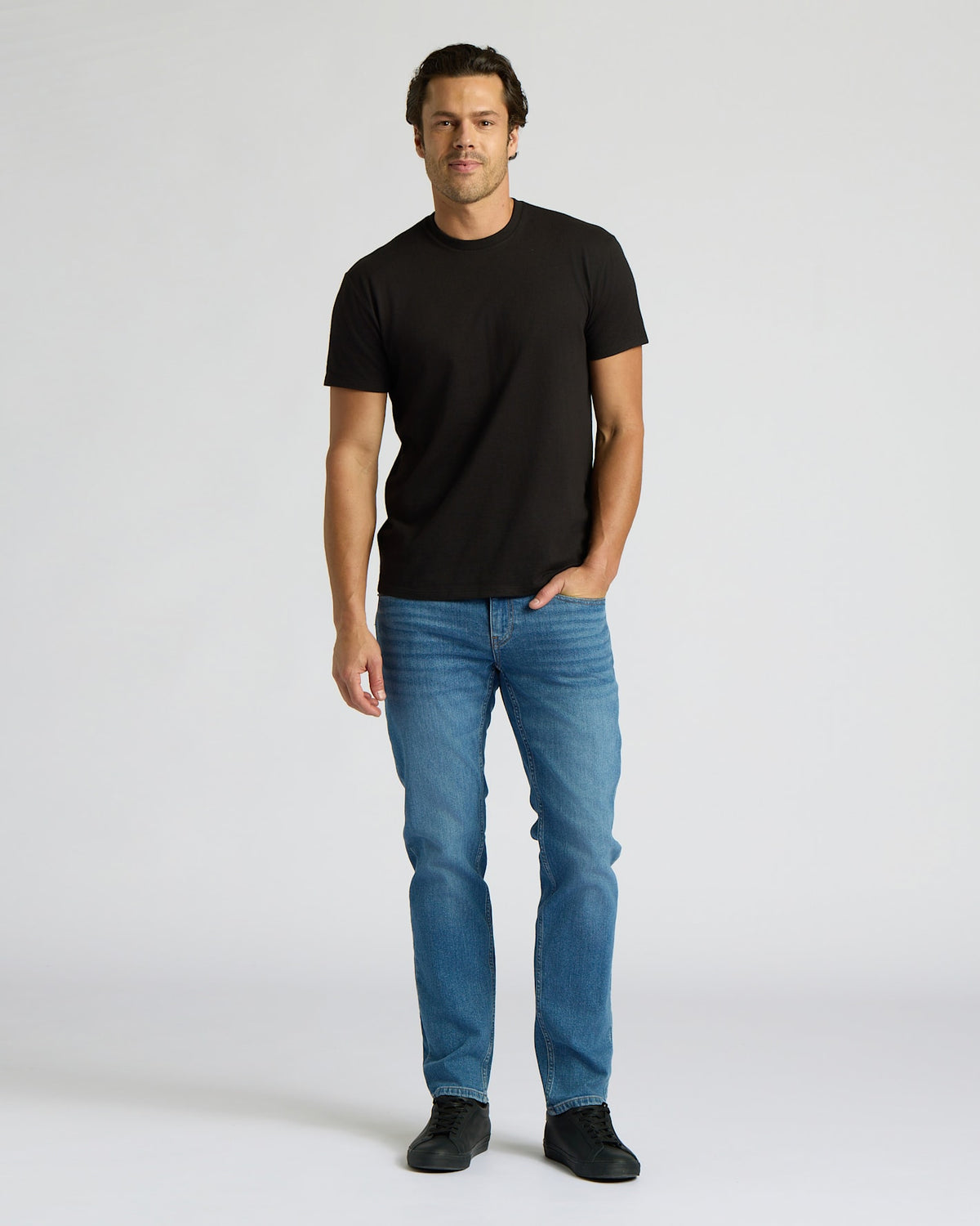 Man wearing a black t-shirt and blue jeans on a white background. MODEL_INFO: Model is 6'0" wearing size L short