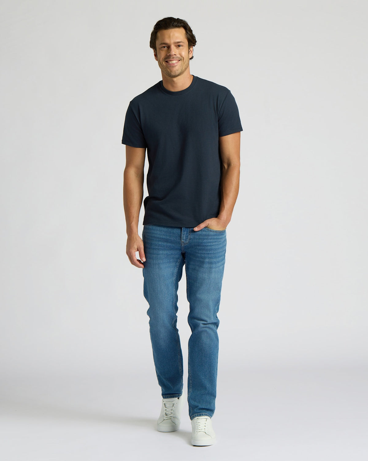 Man wearing a navy t-shirt and blue jeans on a white background. MODEL_INFO: Model is 6'0" wearing size L short