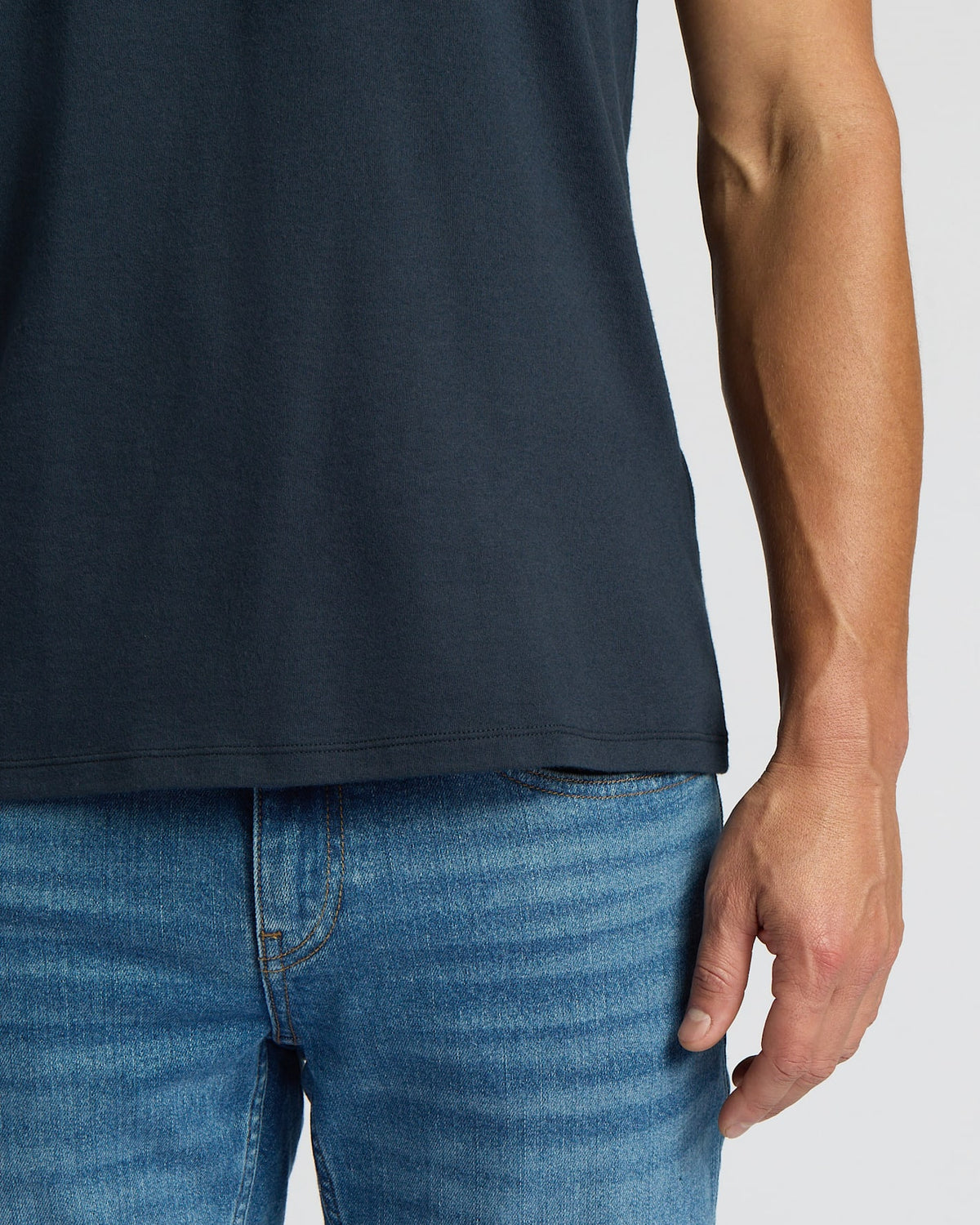 Person wearing a dark blue t-shirt and light blue jeans on a plain background