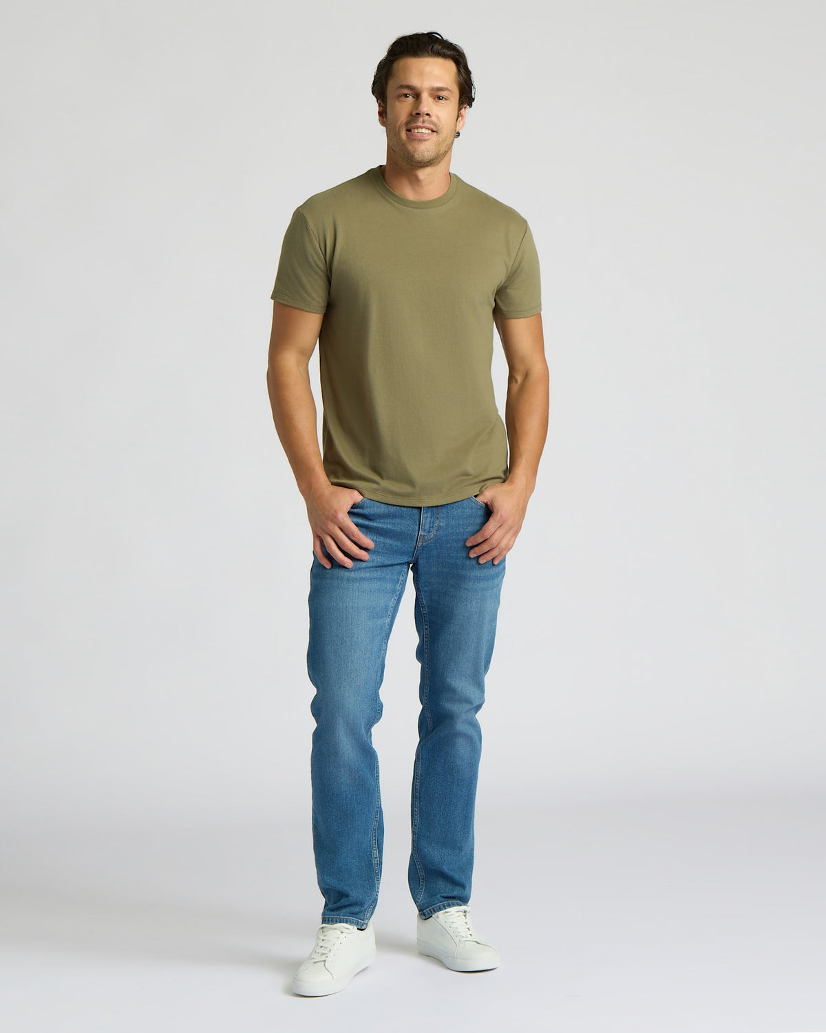 Man wearing an olive green t-shirt and blue jeans on a white background. MODEL_INFO: Model is 6'0" wearing size L short