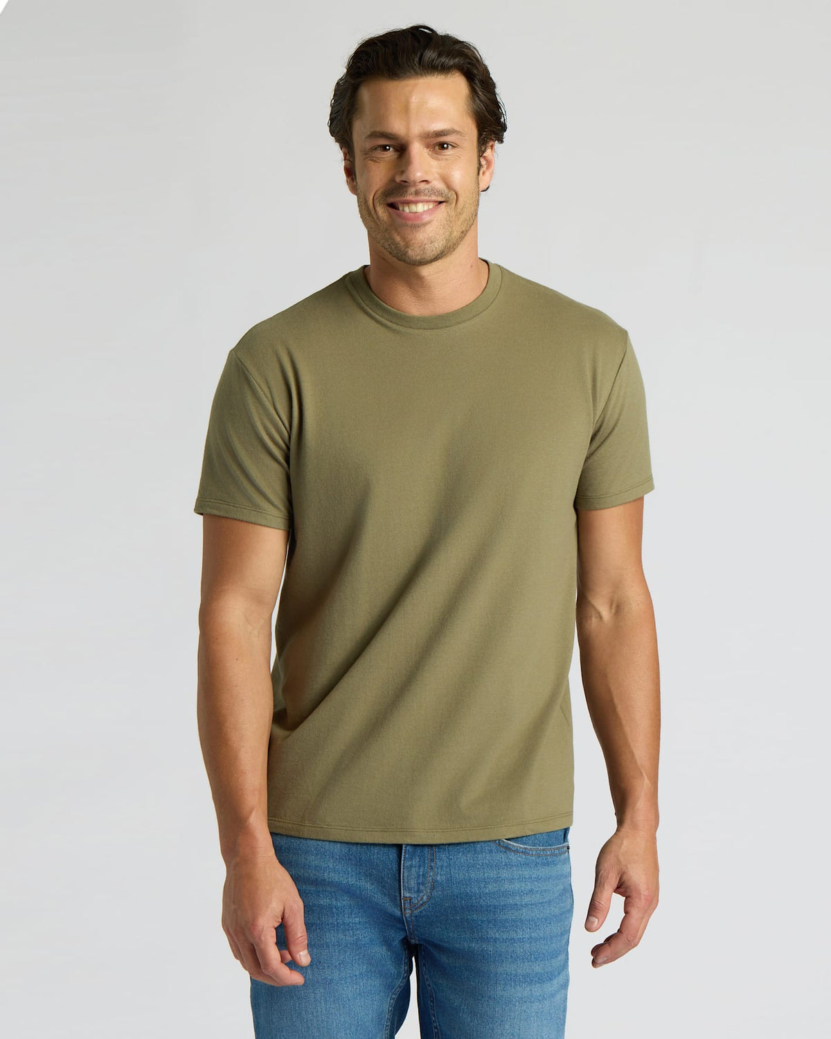 Man wearing an olive green t-shirt and blue jeans on a light gray background