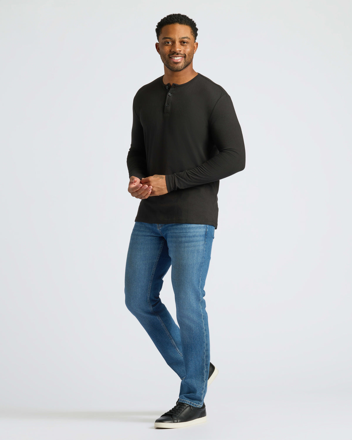 Man wearing Black Long Sleeve Henley with jeans and sneakers.