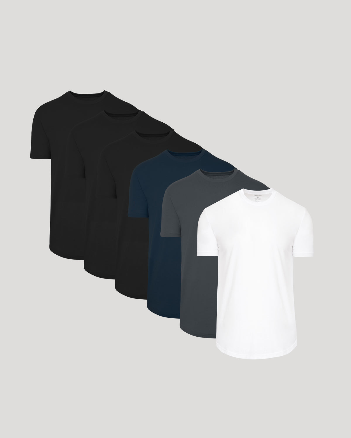 Six short-sleeve crew-neck t-shirts arranged in a diagonal stack on a light gray background, showing color options from black to white.