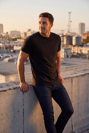 Pima Polish - Pima Crew, Jeans, & Boxers featuring a man in a black crew neck shirt and dark jeans on a rooftop, showcasing men's basics
